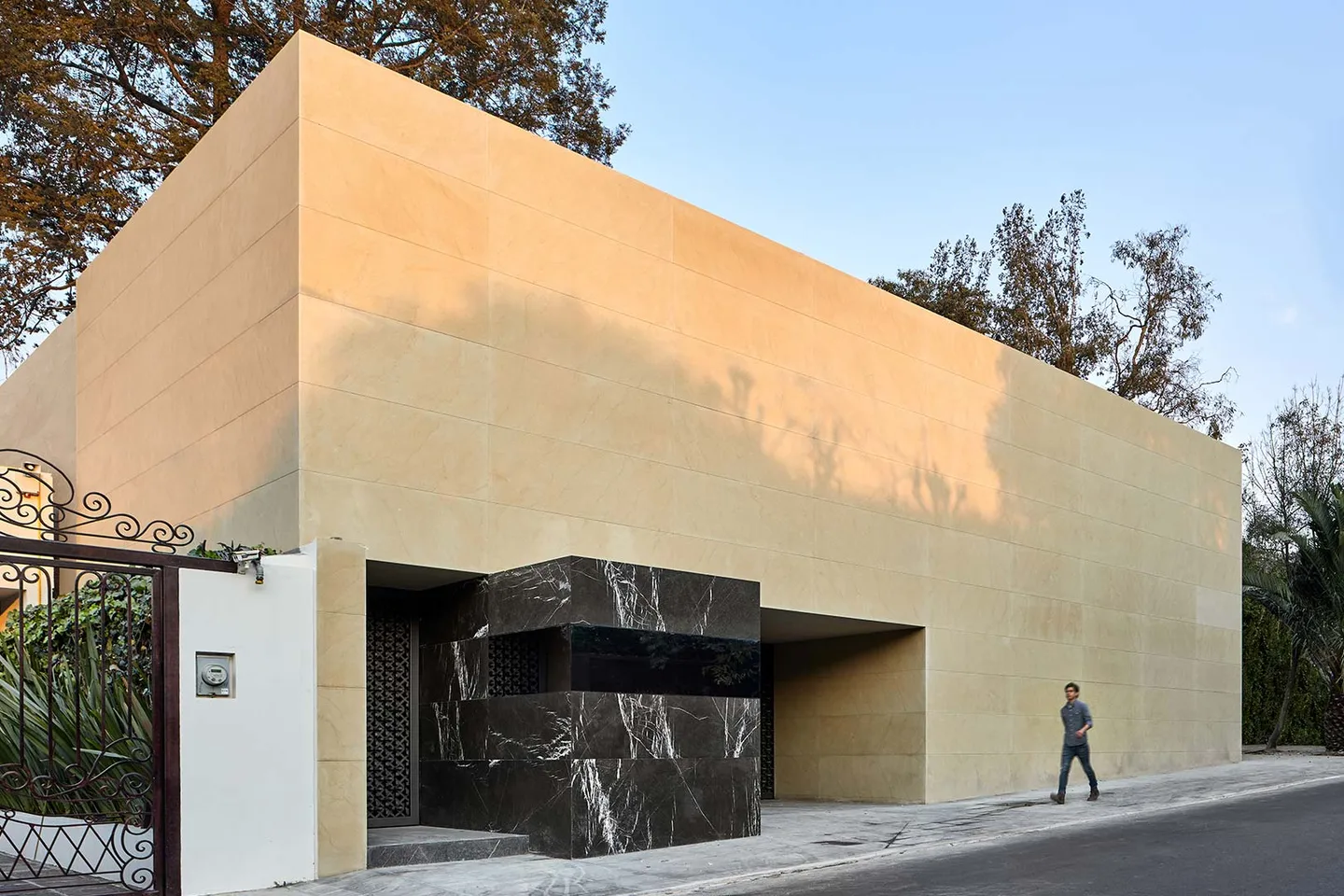 Casa LU: volumen de piedra clara sobre la calle; una persona al pie da la escala