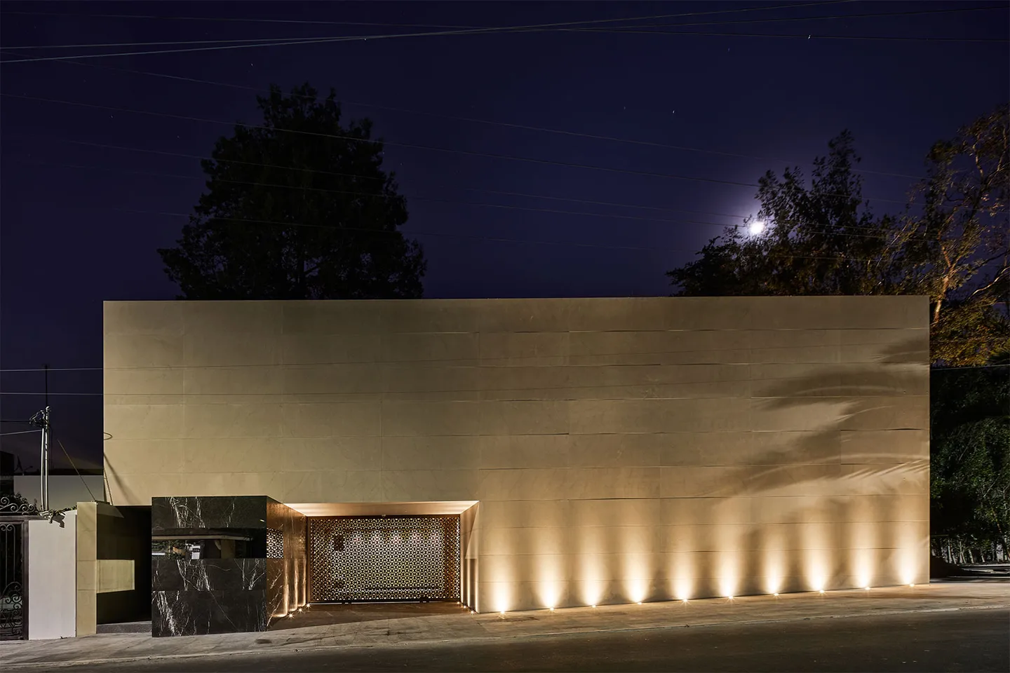 Casa LU: muro de piedra iluminado desde el suelo, de noche