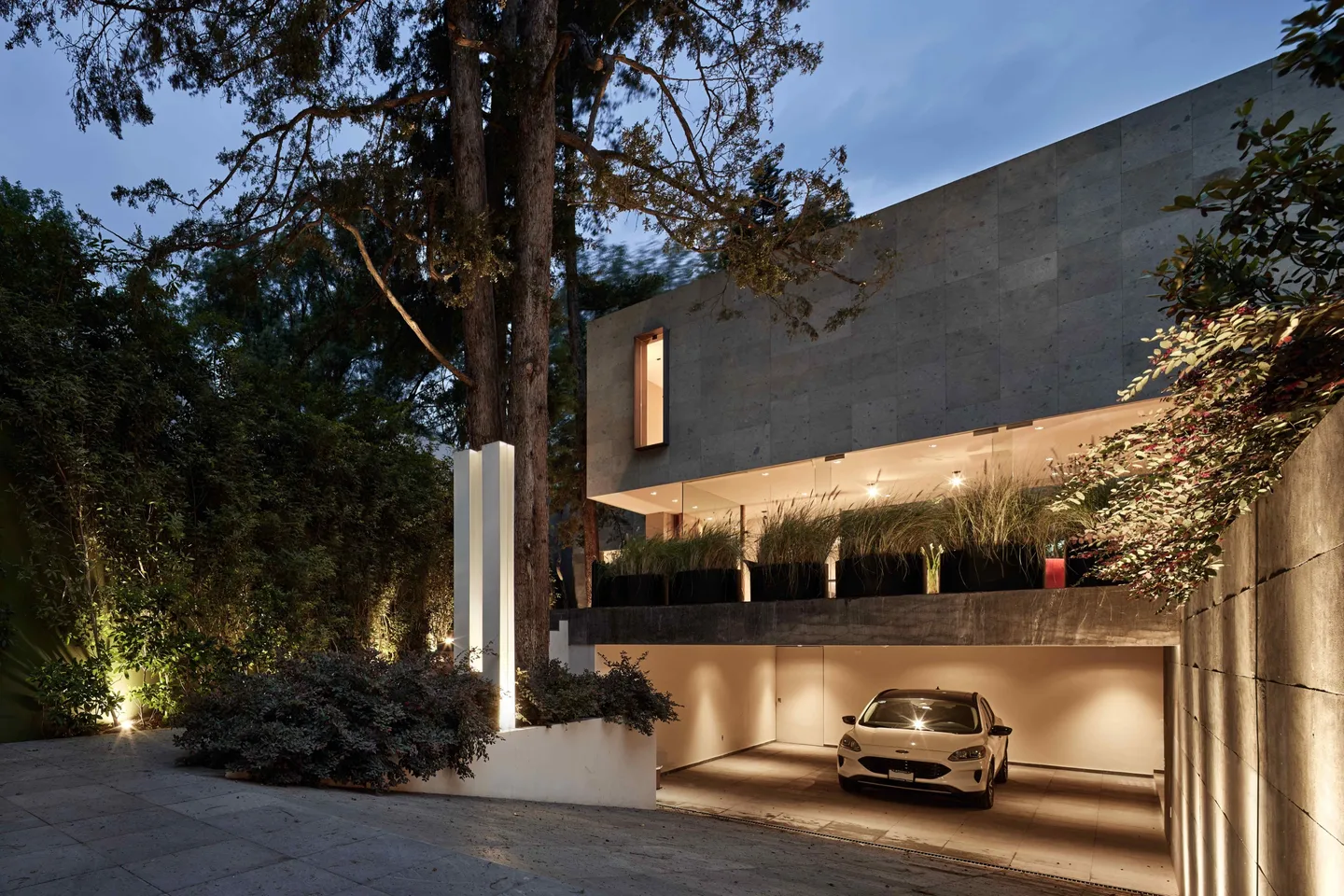 Casa FS: fachada iluminada de noche entre árboles