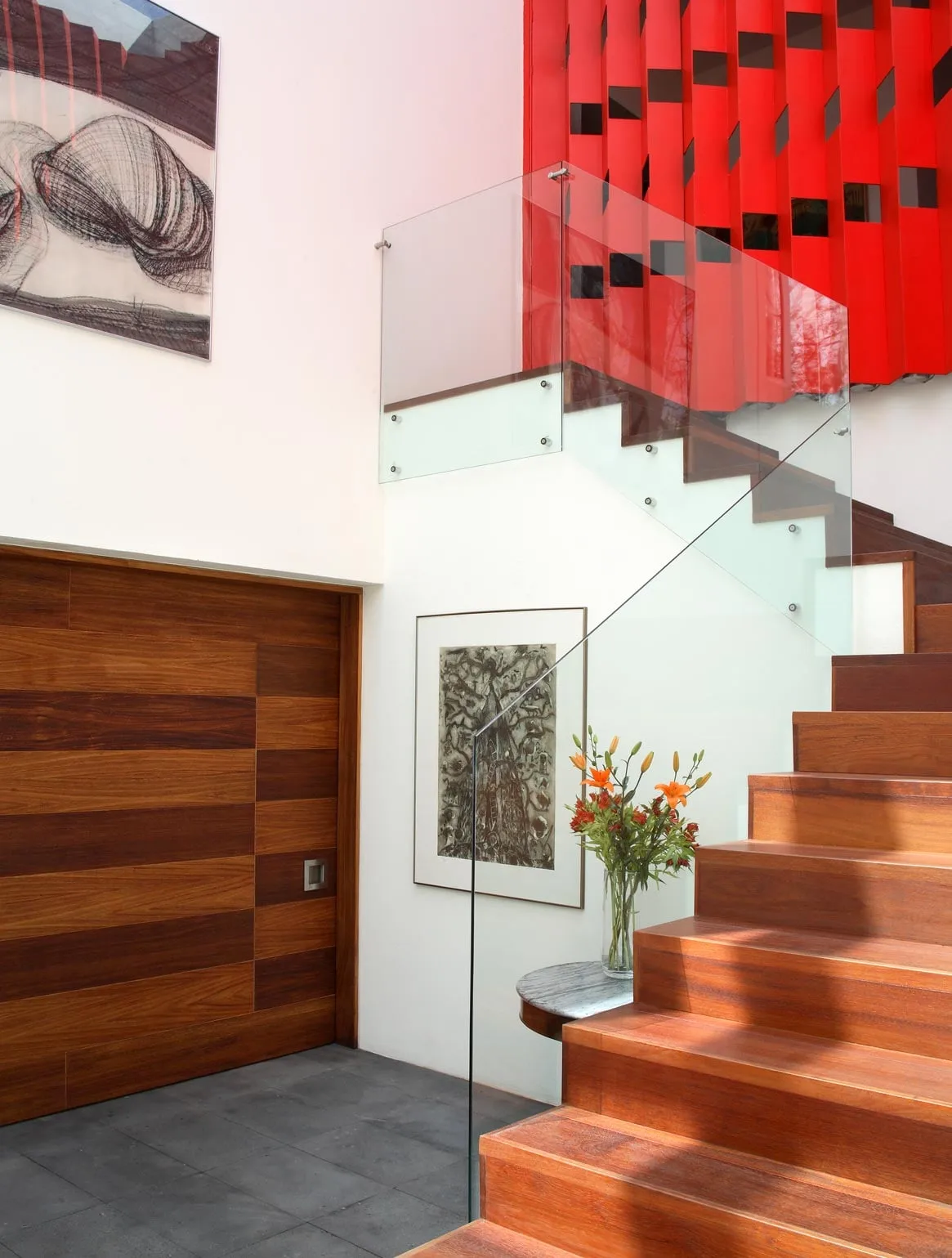 Casa F1: escalera de madera junto a la puerta de acceso, con la celosía roja en lo alto