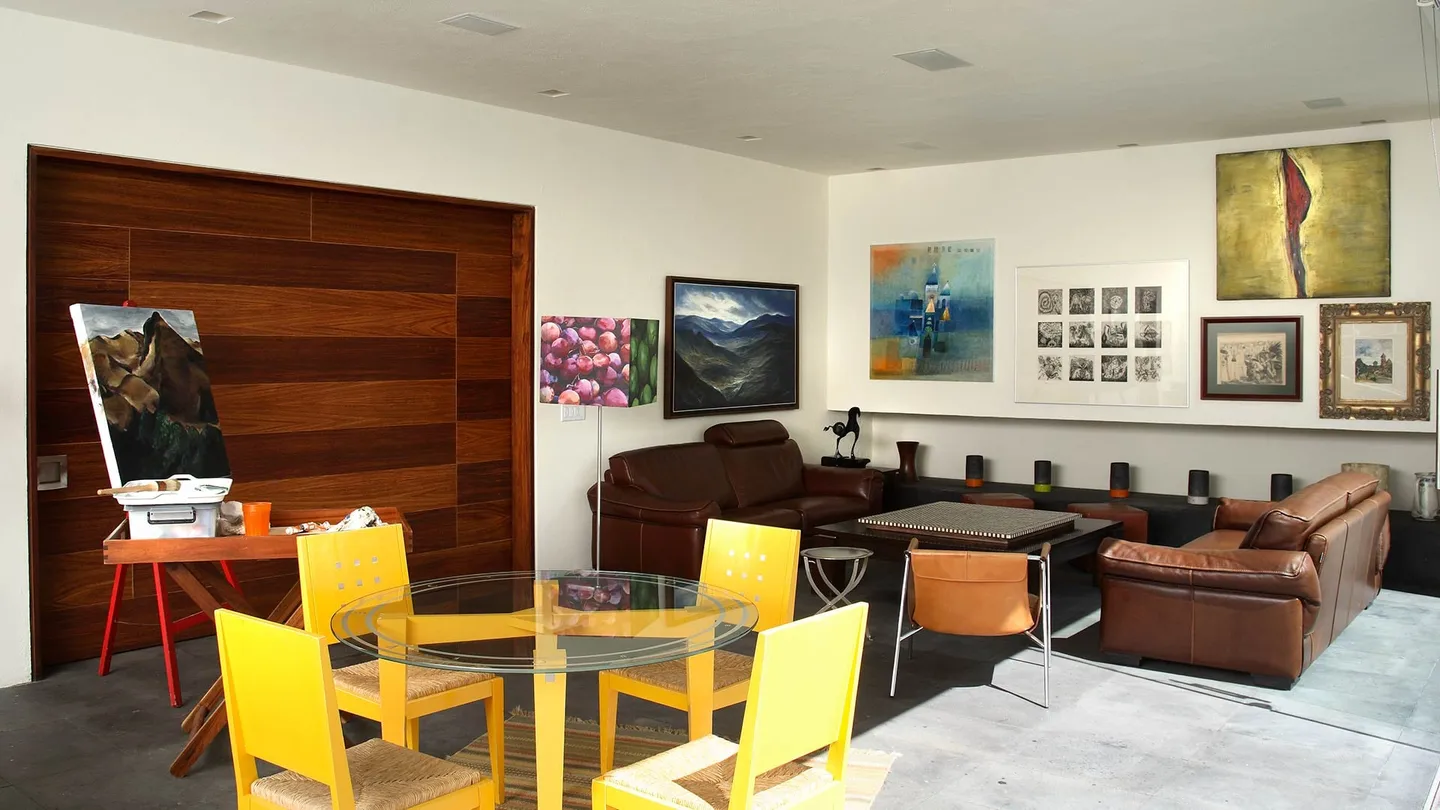Casa F1: estancia con muro de madera, sillas amarillas y obra gráfica en los muros