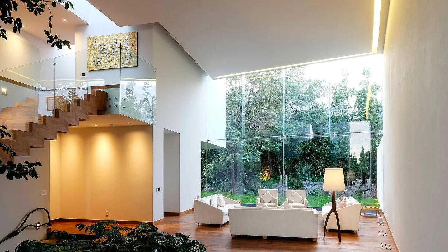Casa AG: estancia a doble altura con escalera de madera y ventanal al jardín