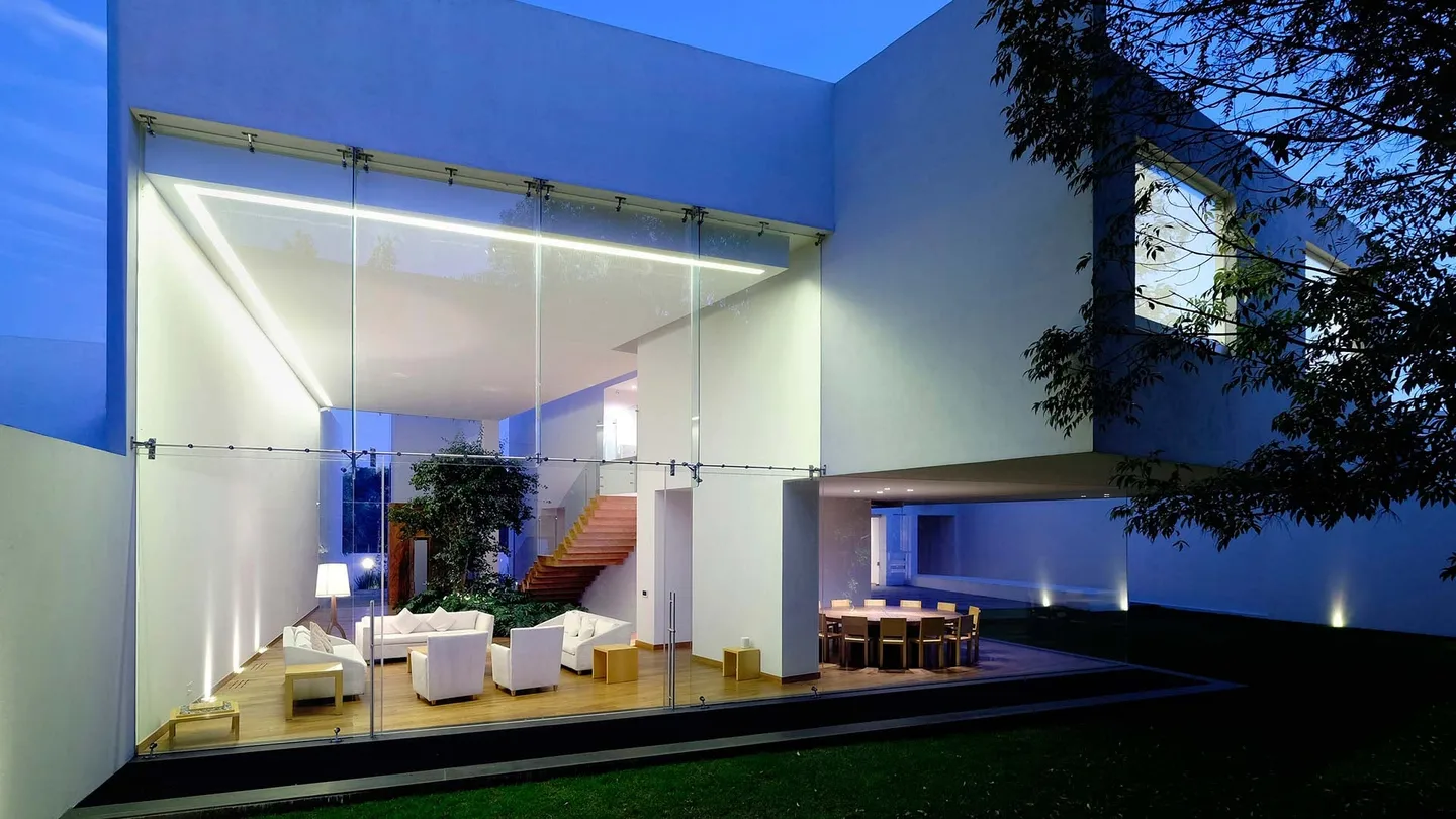 Casa AG: estancia acristalada abierta al jardín en la hora azul