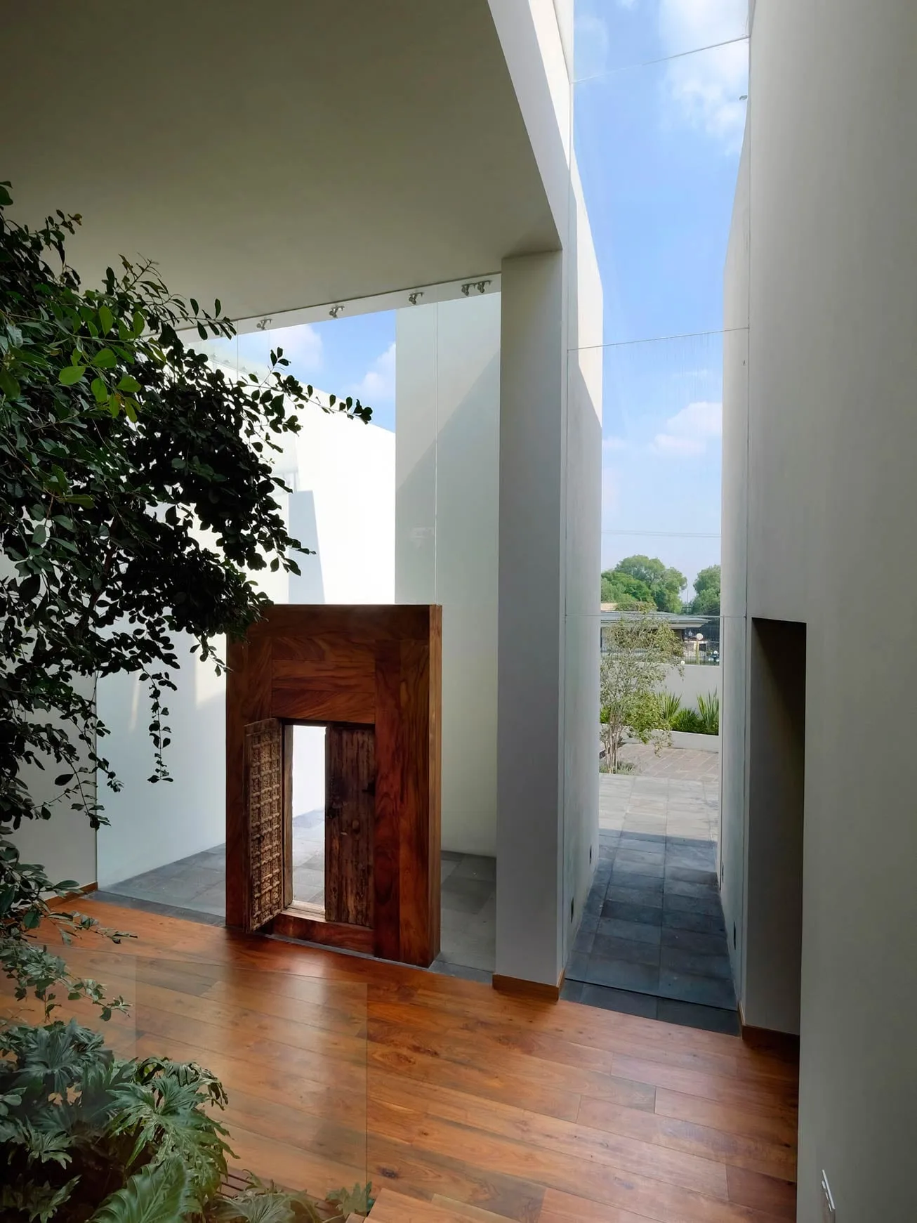 Casa AG: pasillo de muros blancos hacia una puerta de madera