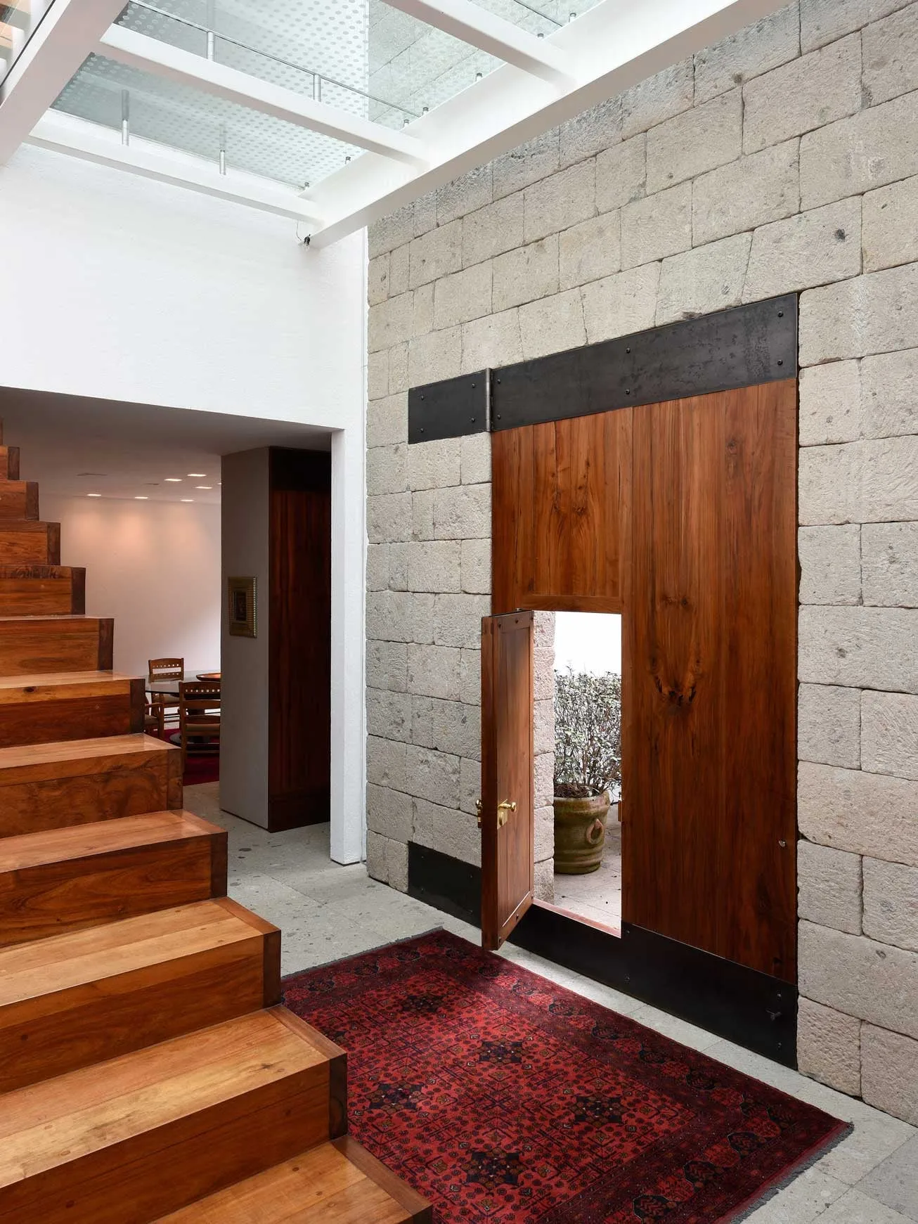 Casa FR: acceso con escalera de madera, muro de block y luz cenital