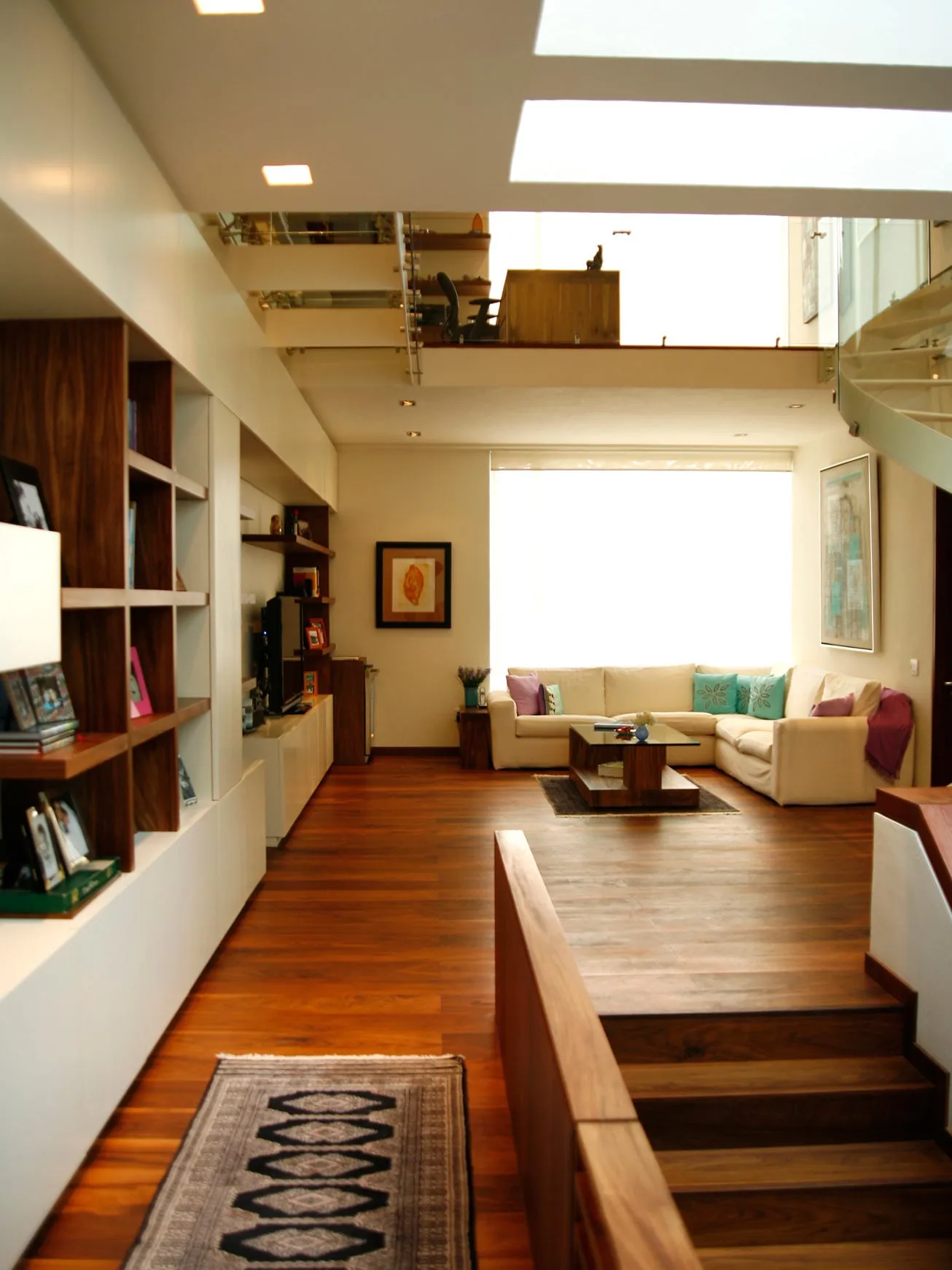 Casa FU: biblioteca y estancia unidas por un piso de madera, bajo un tragaluz