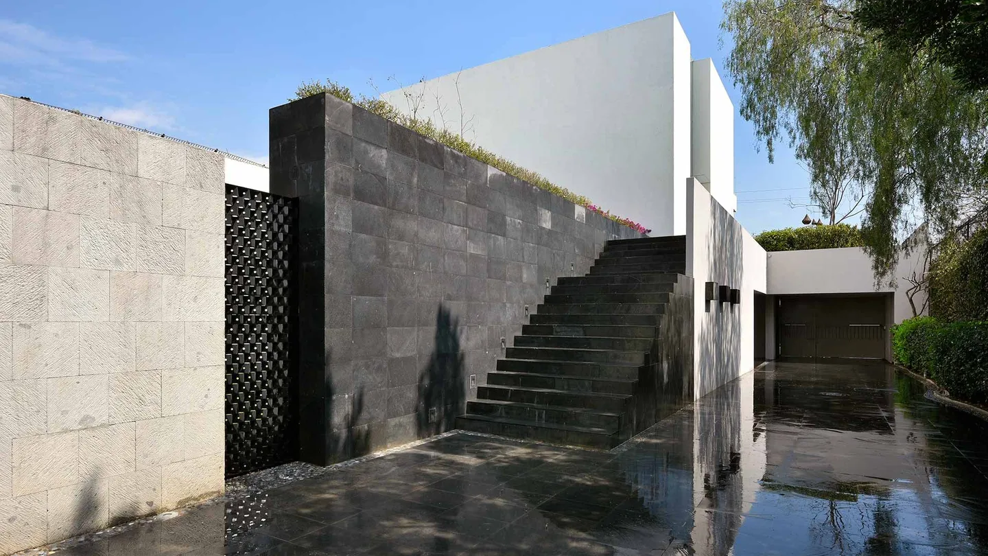 Casa FA: muro de piedra volcánica y escalinata que baja hacia un espejo de agua