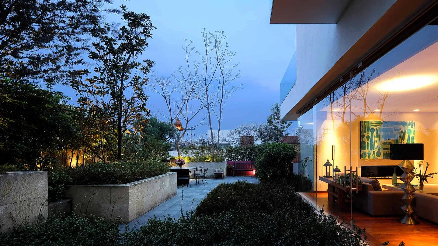Casa FA: terraza ajardinada al atardecer con la estancia iluminada