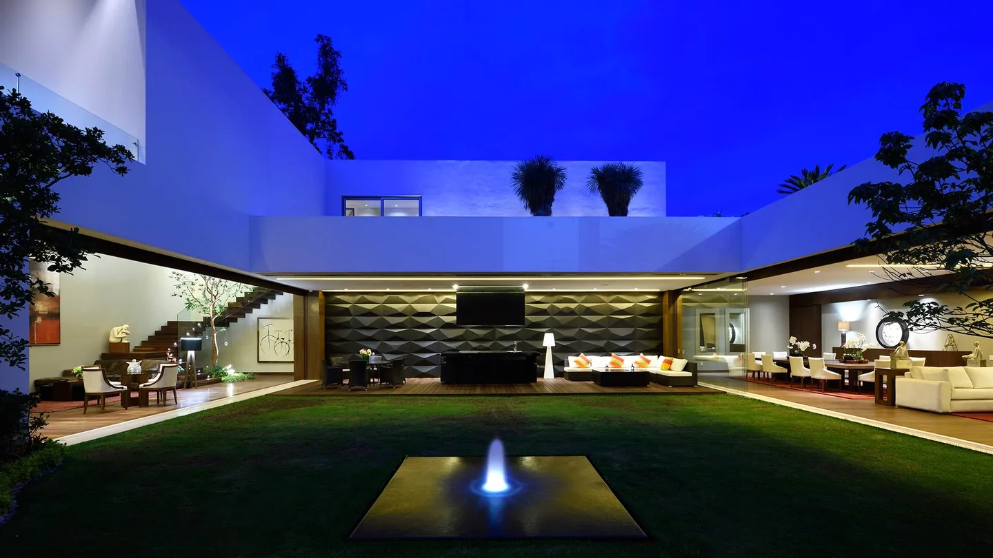 Casa CR: patio central con fuente al anochecer, rodeado por la casa iluminada