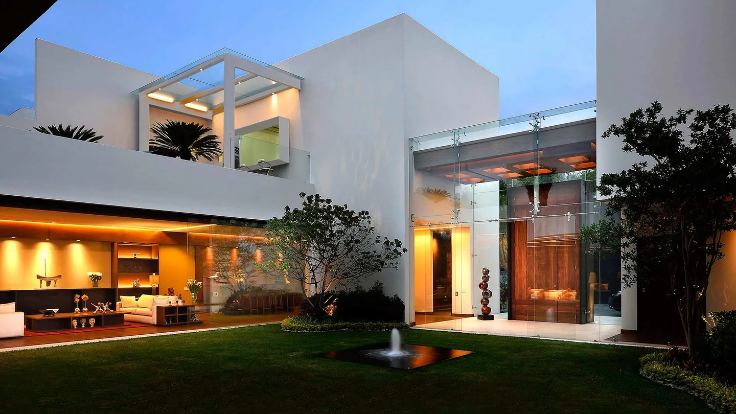 Casa CR: fachada al jardín con terrazas y vestíbulo de vidrio, al anochecer