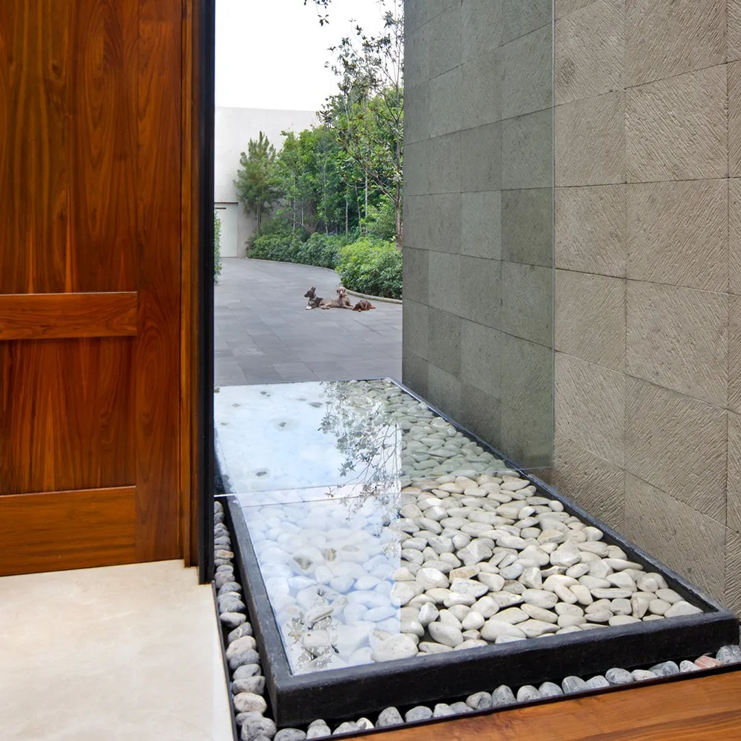 Casa RI: espejo de agua con cantos blancos junto a un muro de piedra