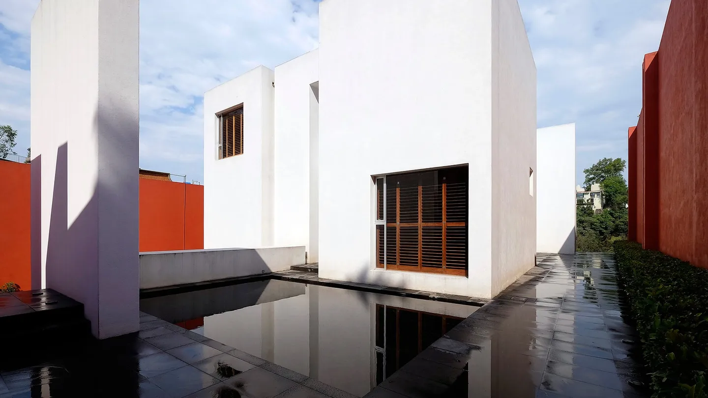 Casa TE: volúmenes blancos alrededor de un espejo de agua, con muros rojos al fondo