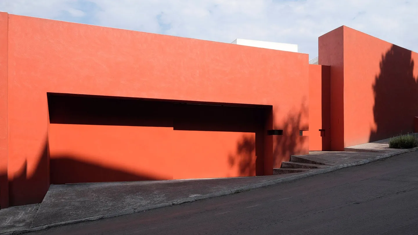 Casa TE: muros rojos del acceso bajo el cielo