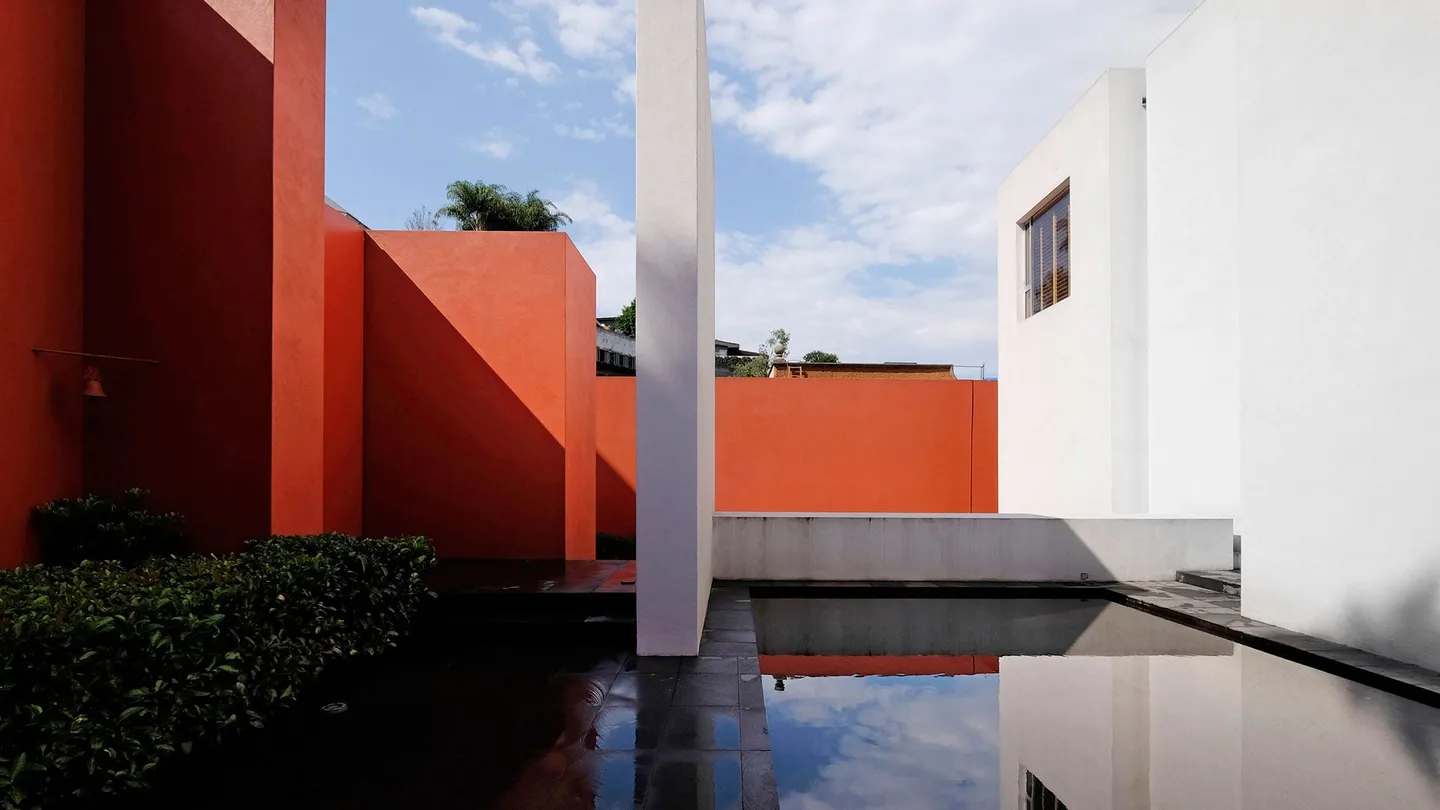 Casa TE: muros rojos y blancos reflejados en el espejo de agua