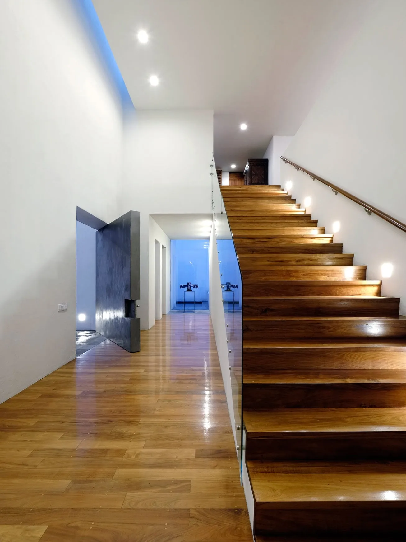 Casa TE: escalera de madera iluminada a lo largo de un pasillo blanco