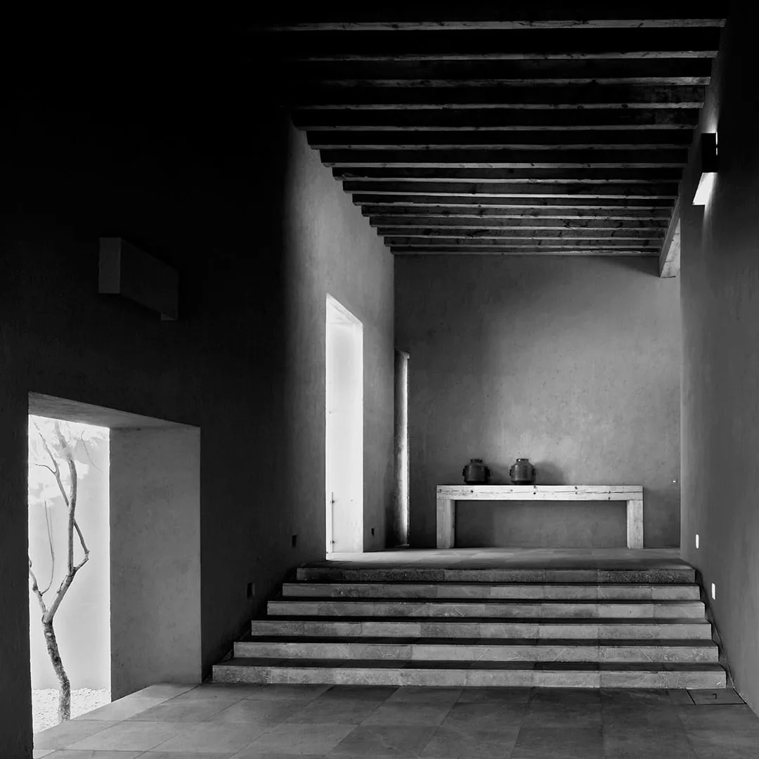 Casa CU 2: vestíbulo de muros grises y escalinata bajo vigas, en blanco y negro