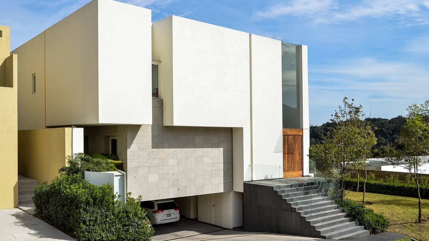 Casa CU: volúmenes blancos y piedra sobre una escalinata, entre árboles