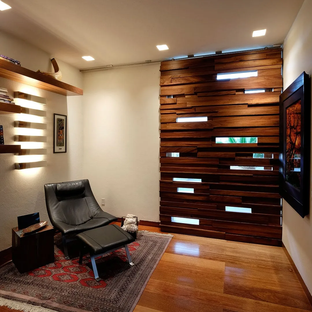 Casa FU3: muro de lamas de madera con ranuras de luz y sillón de lectura