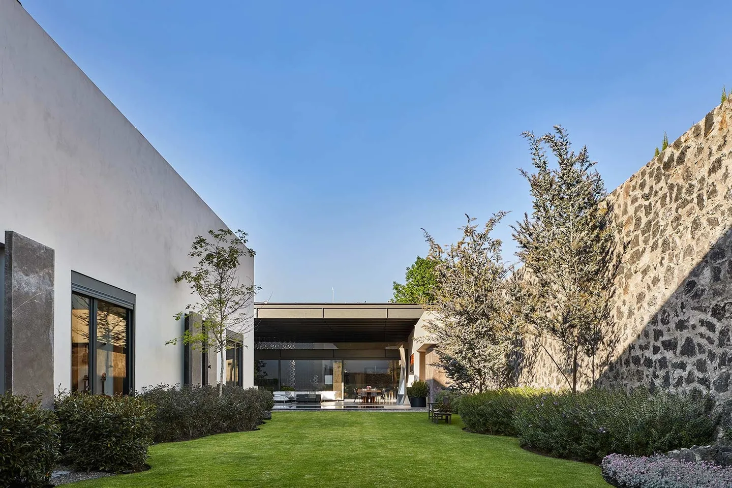 Casa IG: jardín entre un volumen blanco y un muro de piedra volcánica