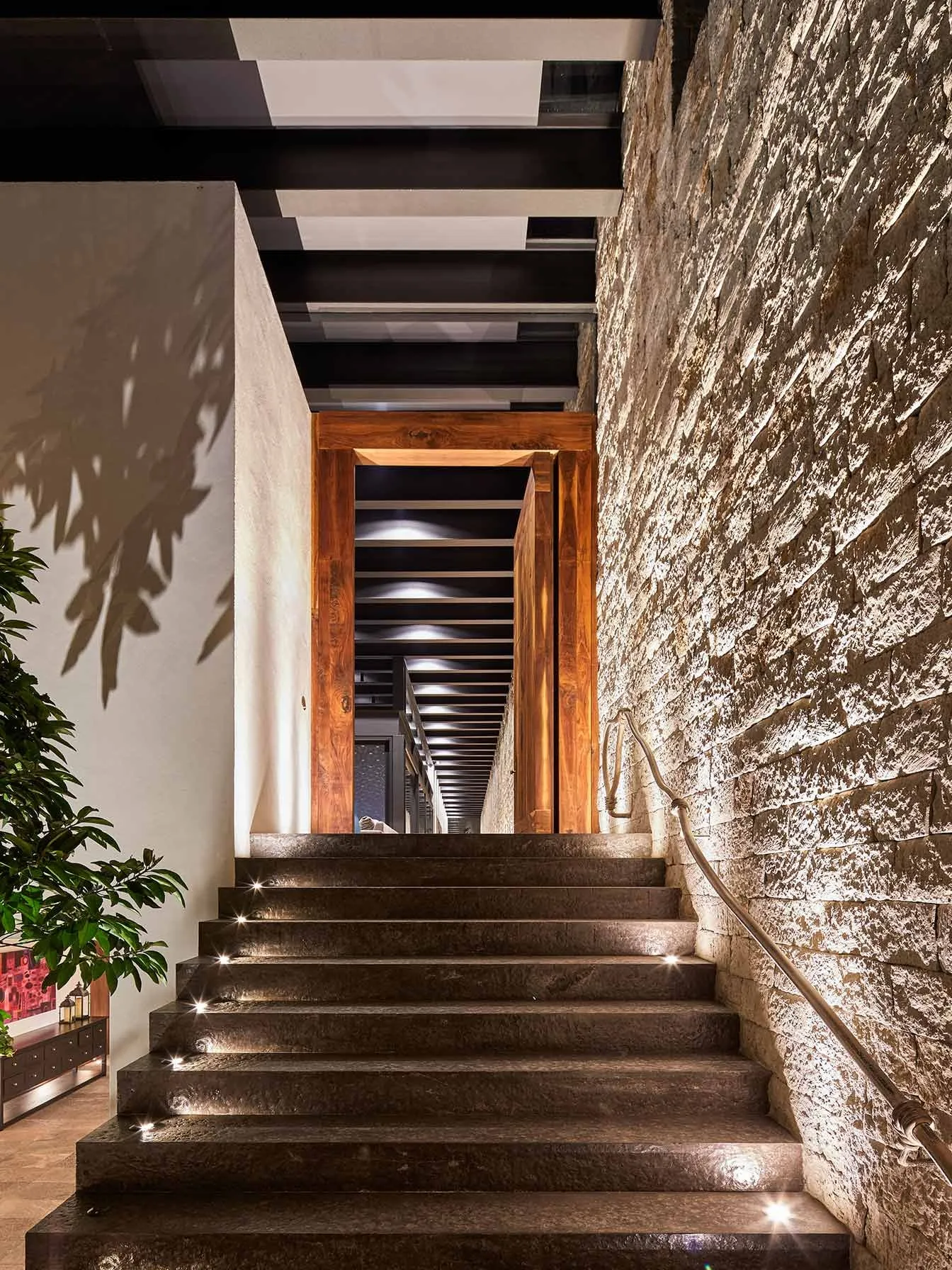 Casa IG: escalera entre muros de piedra hacia una puerta de madera