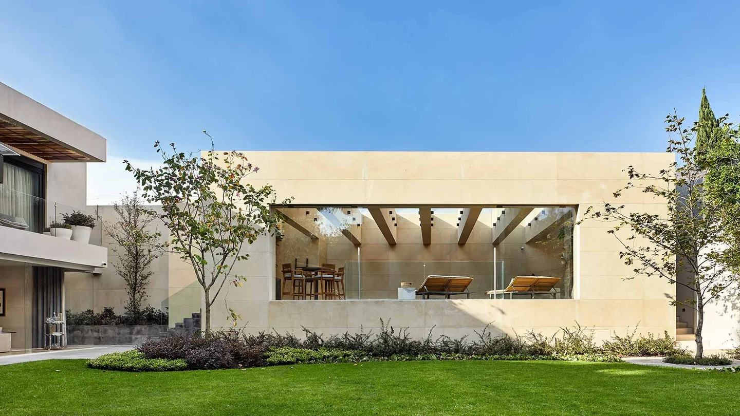 Casa LA: pabellón de piedra clara con ventanal sobre el jardín