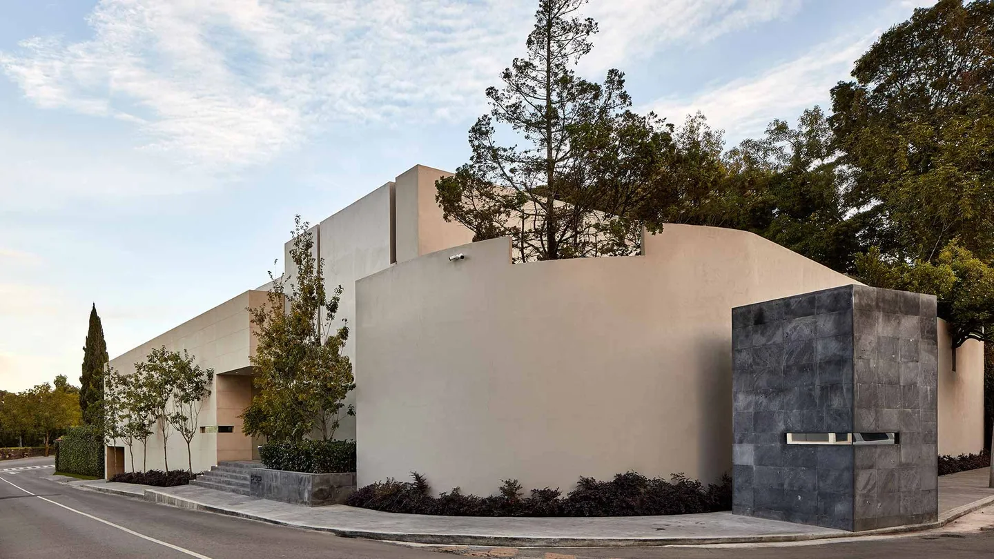 Casa LA: muros claros y piedra oscura del acceso, entre árboles