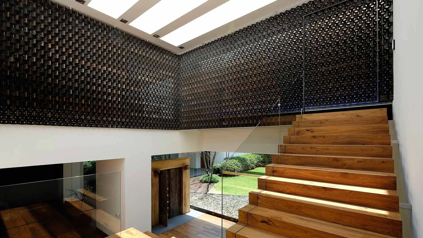 Casa LV: celosía oscura y escalera de madera en la doble altura
