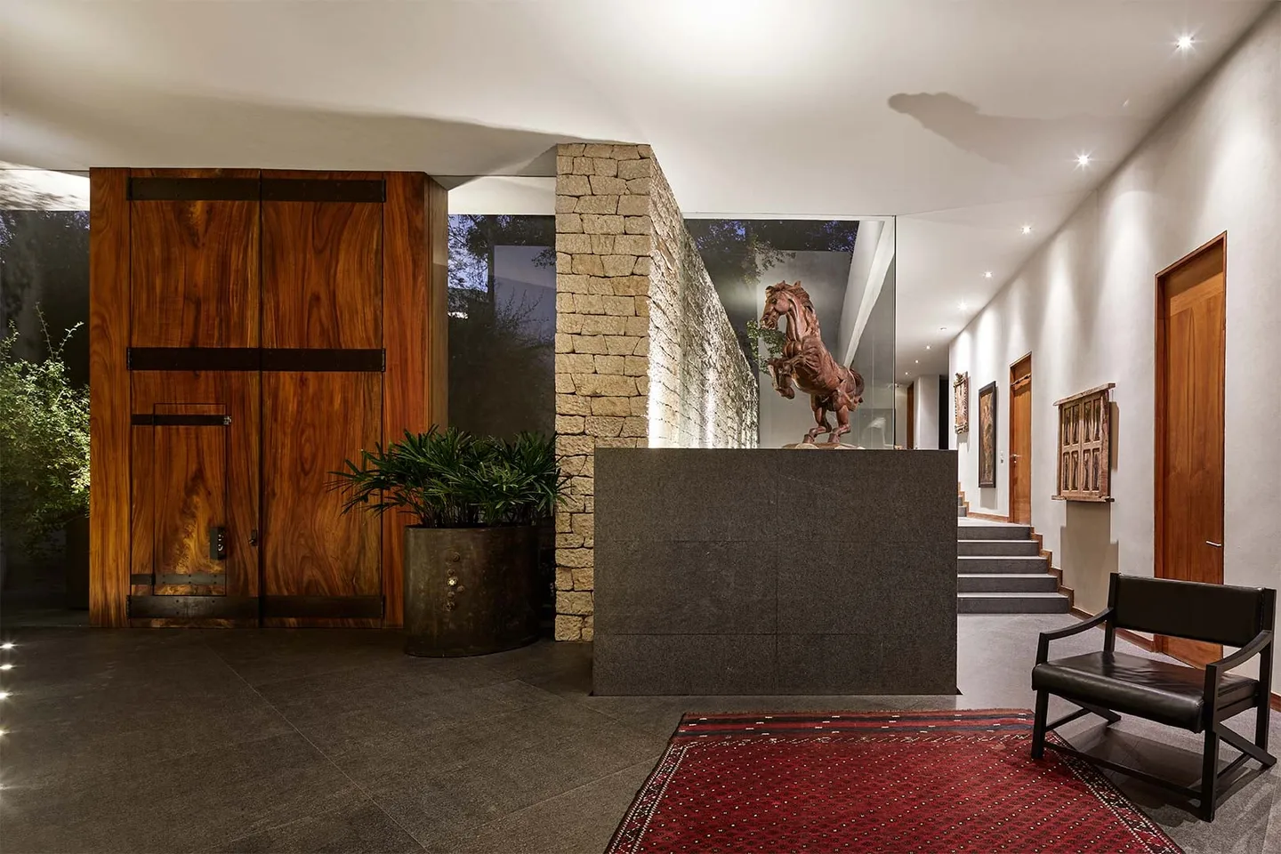 Casa LO: vestíbulo con puerta de madera, muro de piedra y escultura de caballo