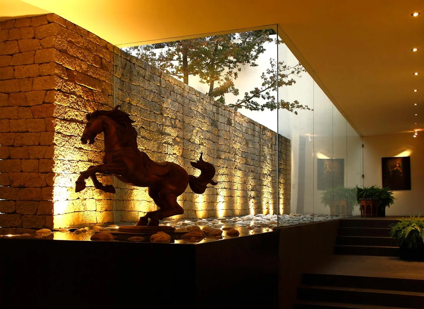Casa LO: muro de piedra iluminado con escultura de caballo y espejo de agua