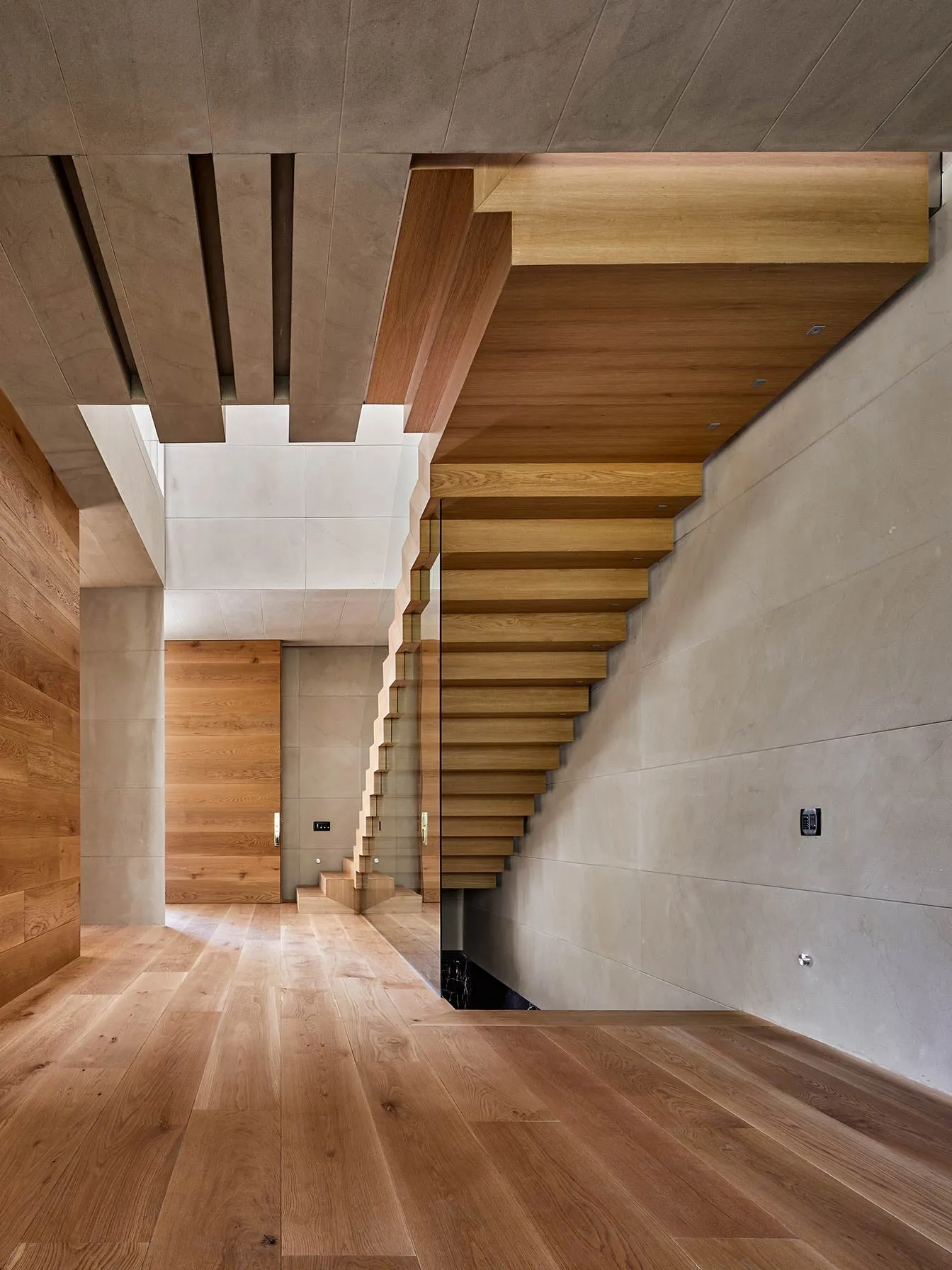 Casa NS: escalera de madera y muro claro en la doble altura