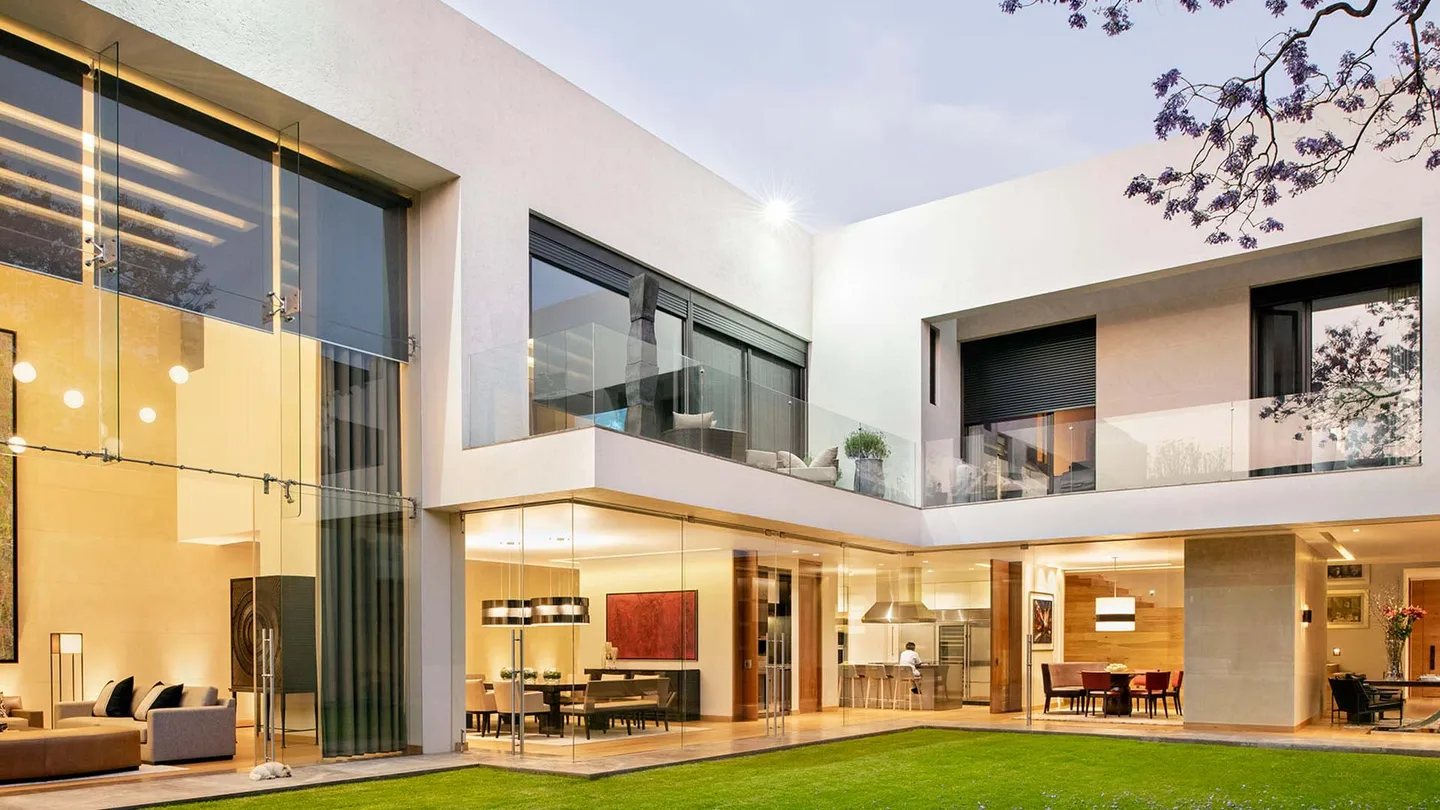Casa OC: fachada de vidrio a doble altura sobre el jardín, al atardecer