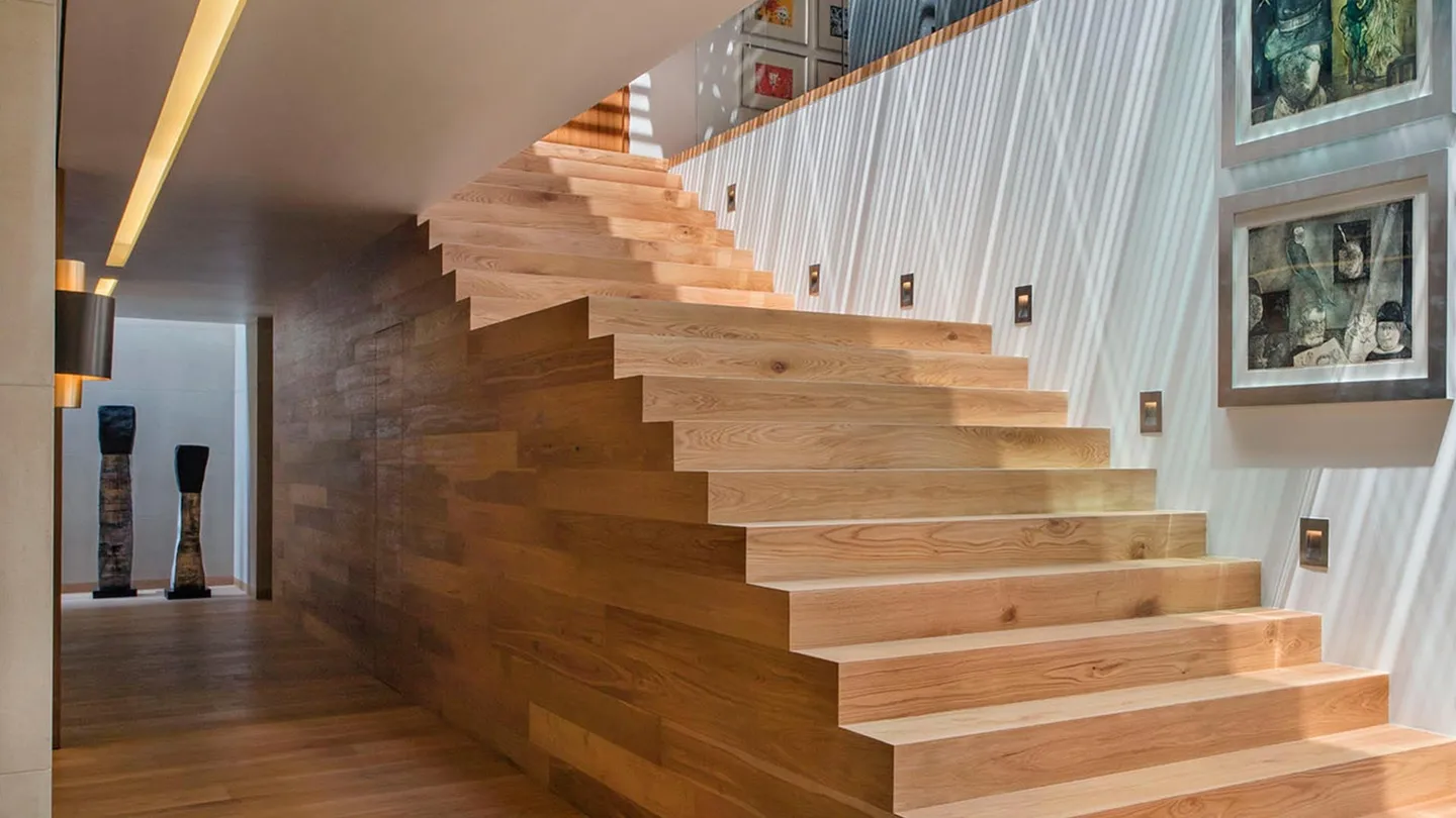 Casa OC: escalera de madera junto a un muro con obra de arte