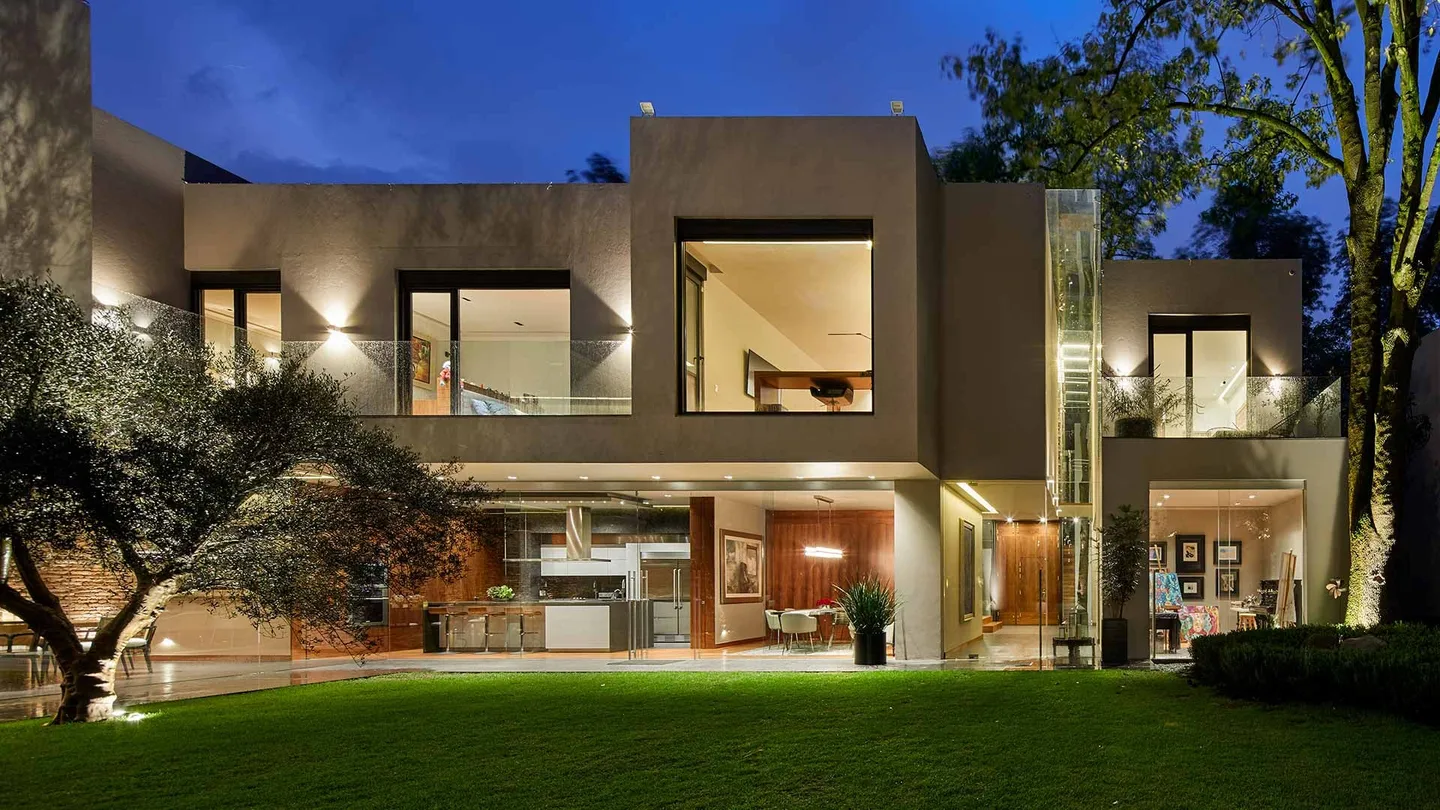 Casa PD: fachada al jardín iluminada en la hora azul, entre olivos