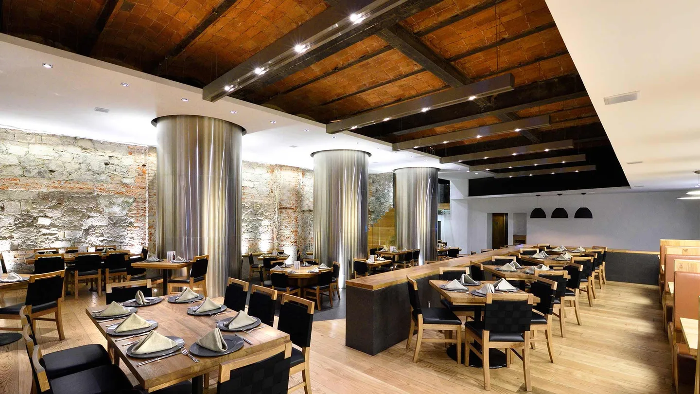 Restaurante 5M: salón con techo de vigas de madera, columnas de acero y muro de piedra