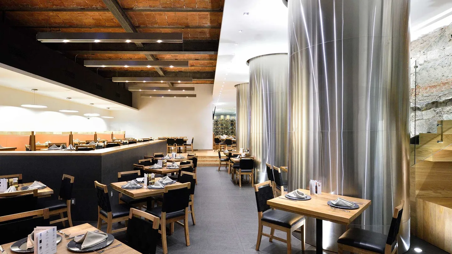 Restaurante 5M: mesas entre columnas de acero bajo las vigas de madera