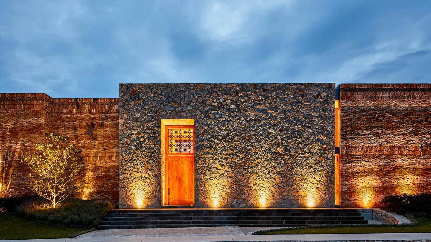Casa SM: fachada de piedra con puerta de madera iluminada al anochecer