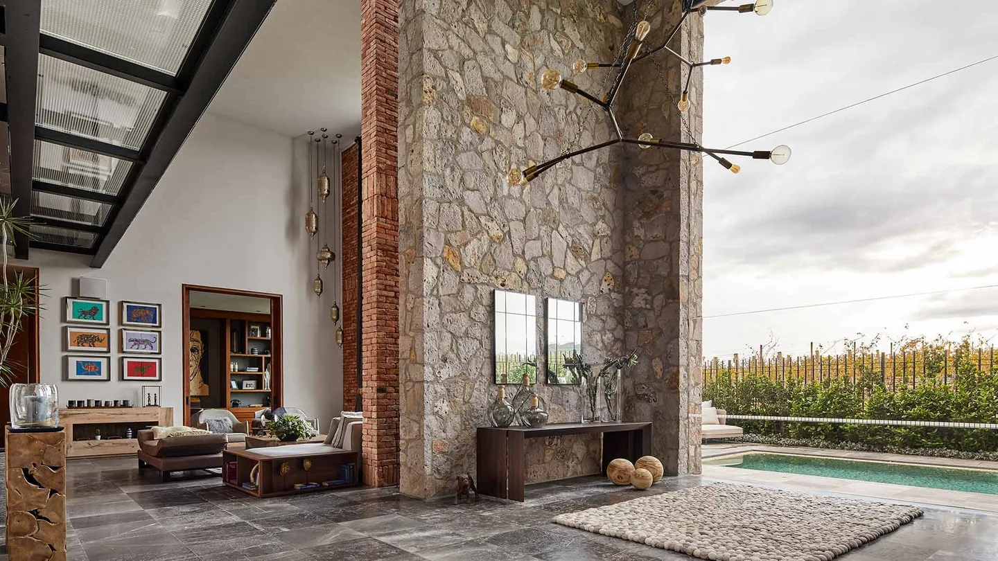 Casa SM: estancia con muro de piedra y ventanal hacia la alberca