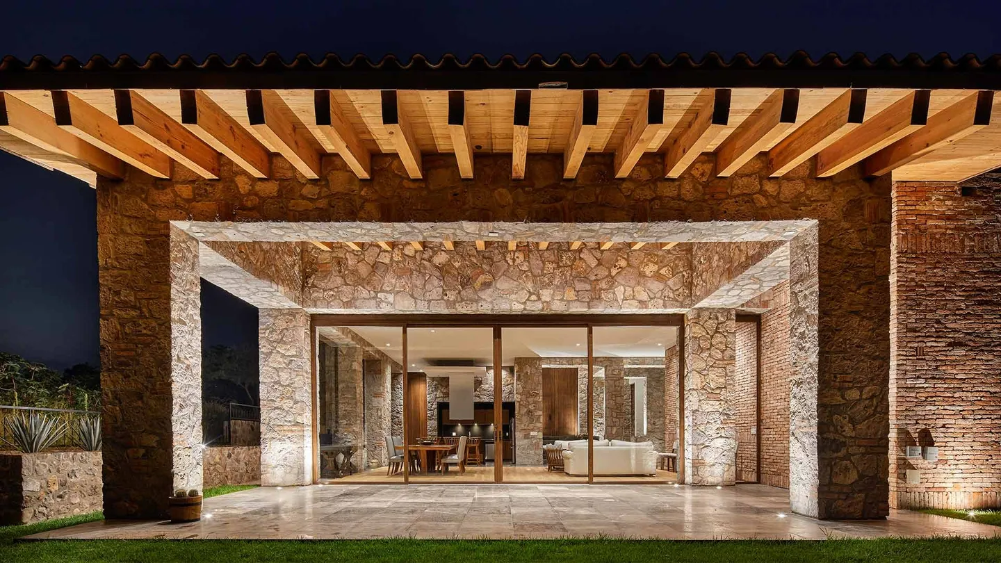Casa SM: pórtico de vigas de madera y marco de piedra, de noche