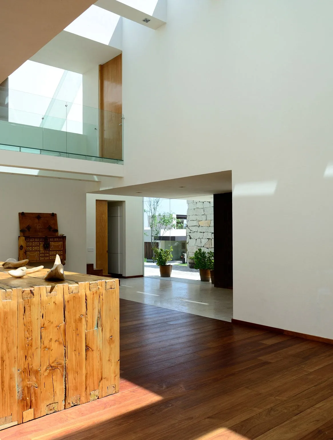 Casa VE: luz cenital sobre un mueble de madera en la doble altura